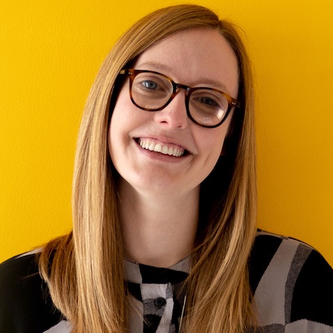 Emma smiling against a yellow background. She’s wearing glasses and has long straight hair.