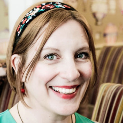 A close-up of Lizzie smiling brightly, her hair matching the blurred background.