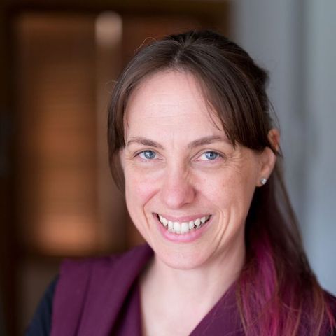 A portrait of Sarah smiling, wearing a top that matches her hair colour.