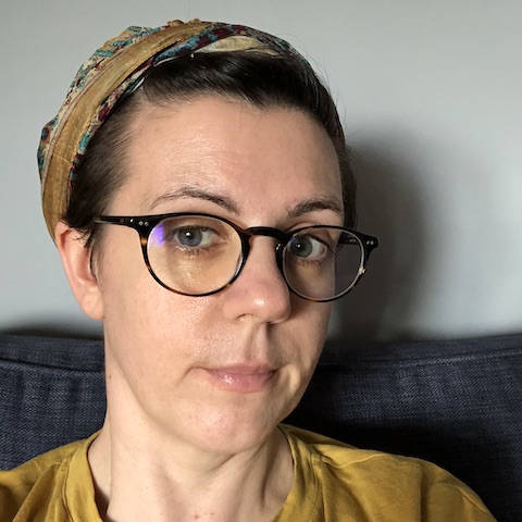A close-up selfie of Stephanie wearing glasses with their hair tied back.