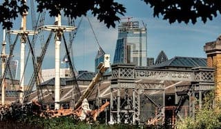 The exterior of the venue with a ship in the foreground and the skyline of London in the background.